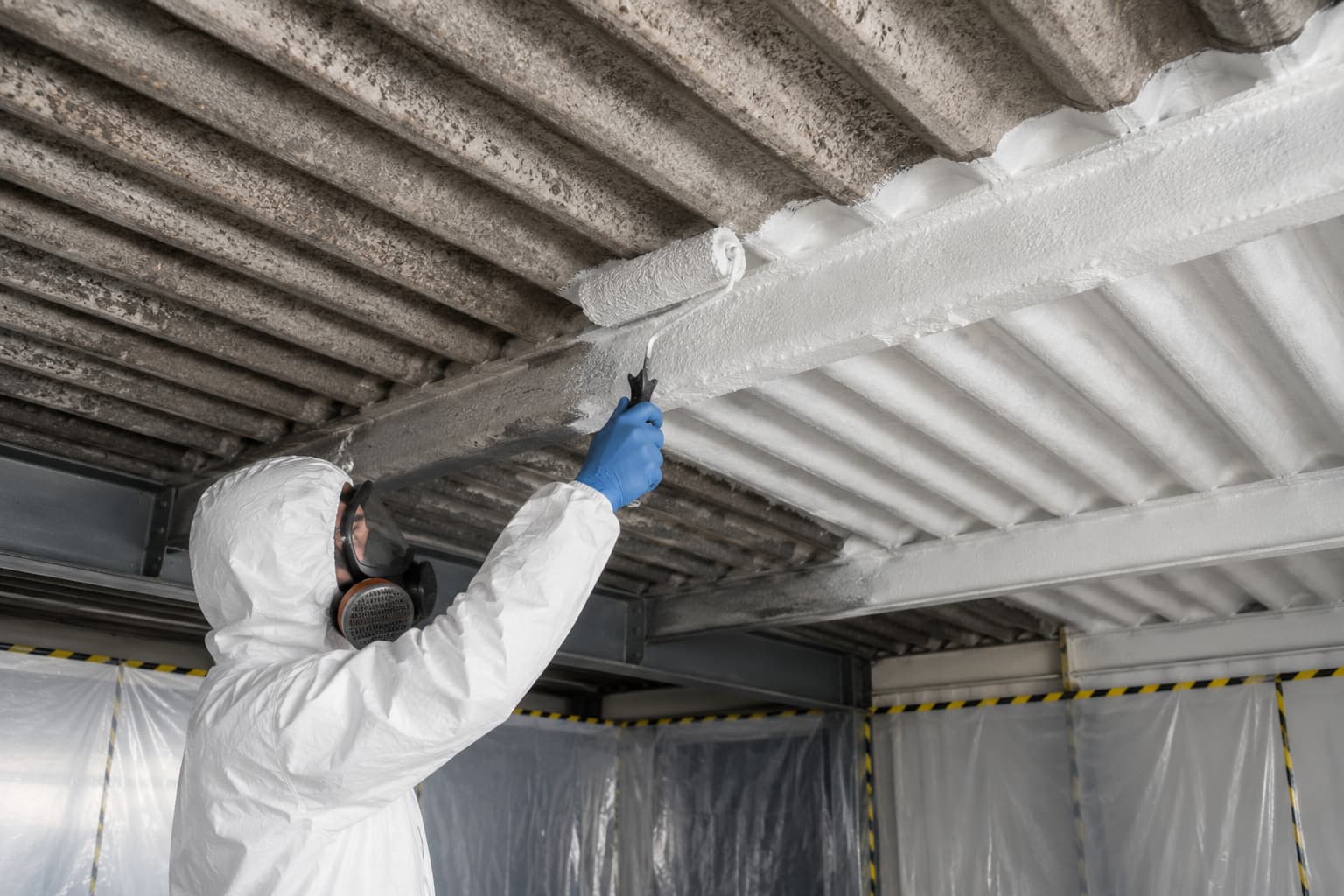 Licensed operative in full PPE applying polymeric sealant to asbestos cement roof sheets during encapsulation works in Surrey