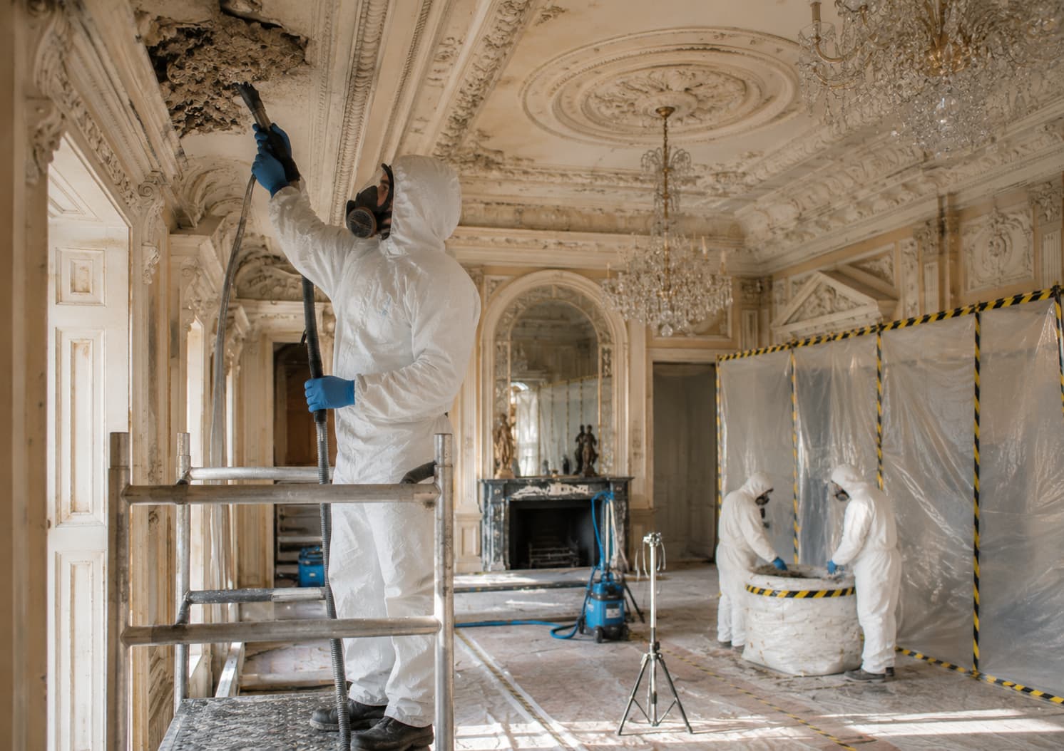 UKATA-trained operatives in full PPE removing asbestos textured coating from a ceiling in a Surrey residential property with containment controls in place