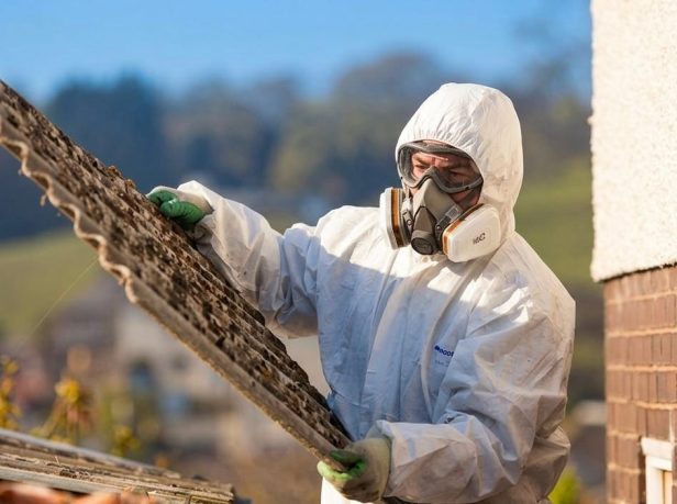 UKATA-trained operative in full PPE carefully lifting a degraded corrugated asbestos cement sheet from a Surrey residential property