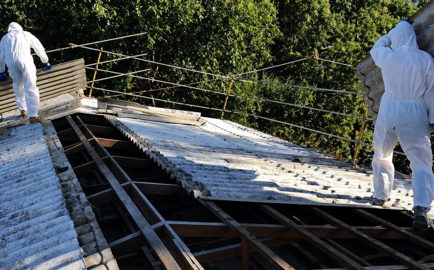 UKATA-trained operatives in full PPE dismantling and removing corrugated asbestos cement sheets from a garage roof.