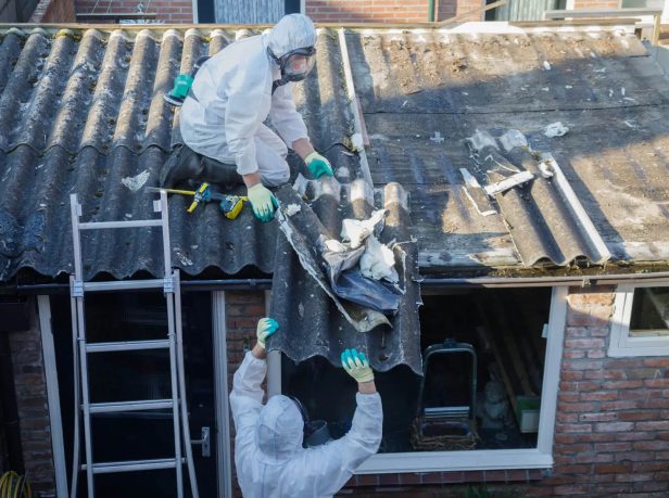 Two UKATA-trained Surrey Asbestos operatives in full PPE working together to carefully remove degraded asbestos cement roof sheets from a residential property in Surrey