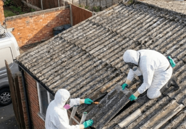Two UKATA-trained Surrey Asbestos operatives in full PPE carefully removing degraded asbestos cement sheets from a domestic garage roof in Surrey