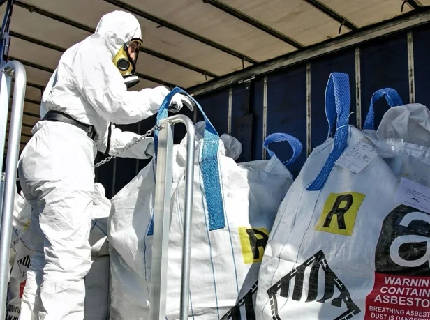 An asbestos disposal specialist loading legally labeled, double-bagged hazardous asbestos waste into a transport vehicle for delivery to a licensed waste facility in Surrey.